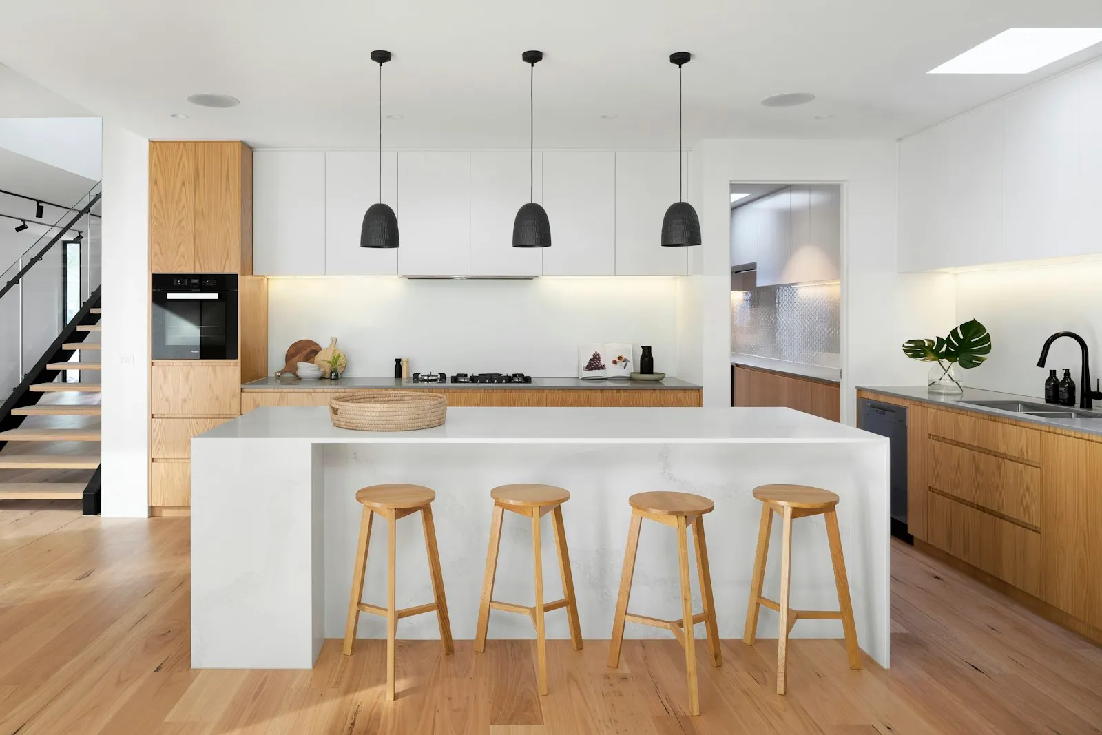 Dapur island minimalis dengan kabinet putih dan kayu, lampu gantung, dan kursi bar kayu