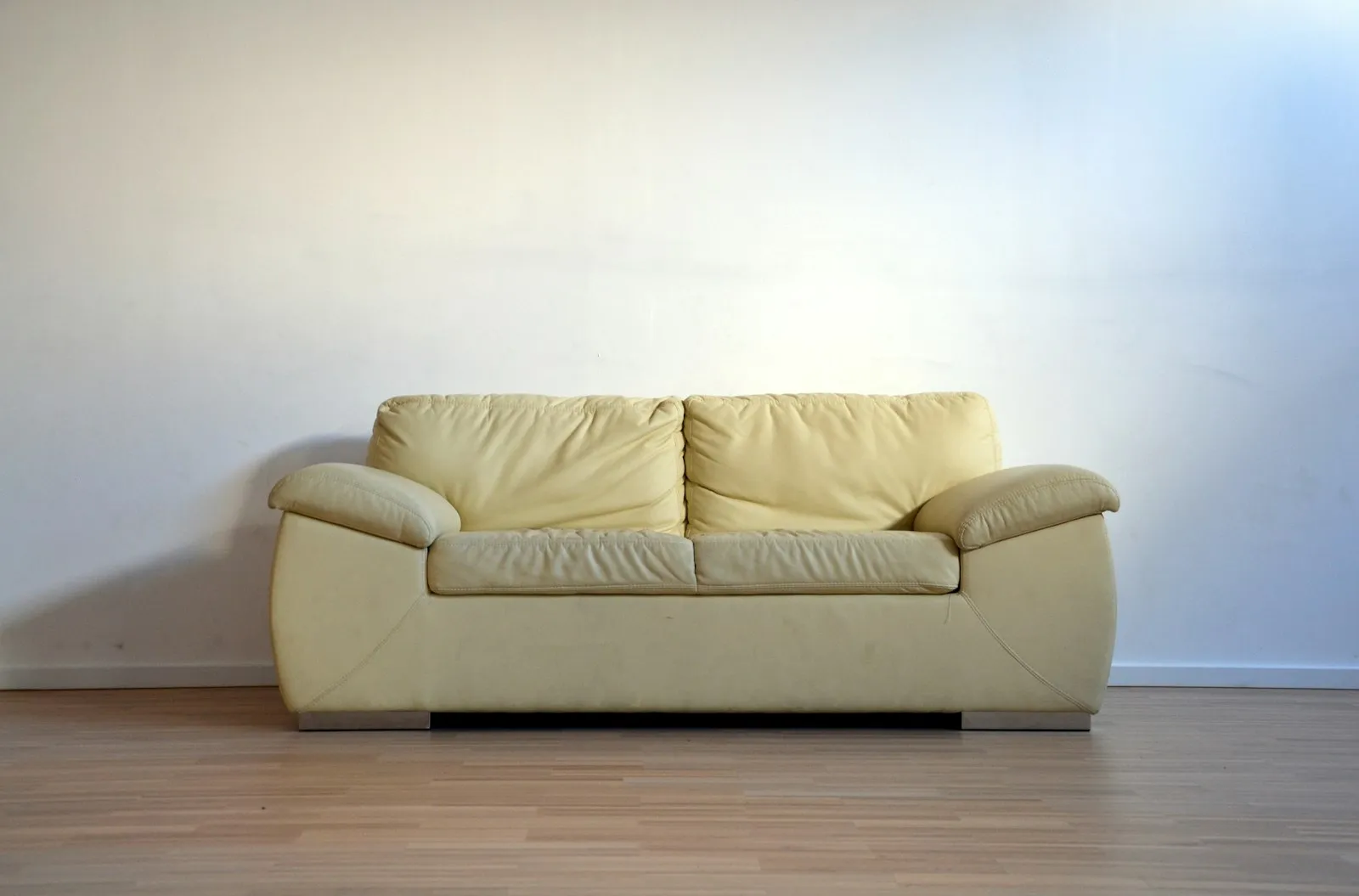 Ruang tamu lama dengan sofa krem usang dan dinding polos tanpa dekorasi