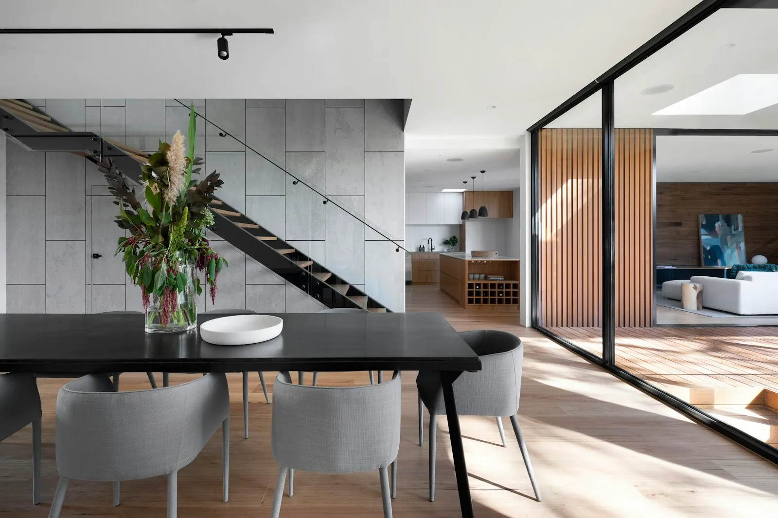 Ruang makan dengan meja hitam, tangga terbuka, dan dinding beton ekspos berlatar interior modern